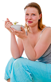 A lady who is smiling whilst eating salad.
